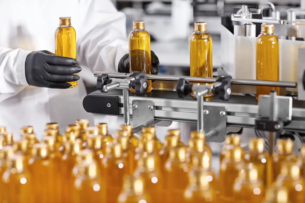 Worker in lab coat inspecting amber bottles on a personal care production line